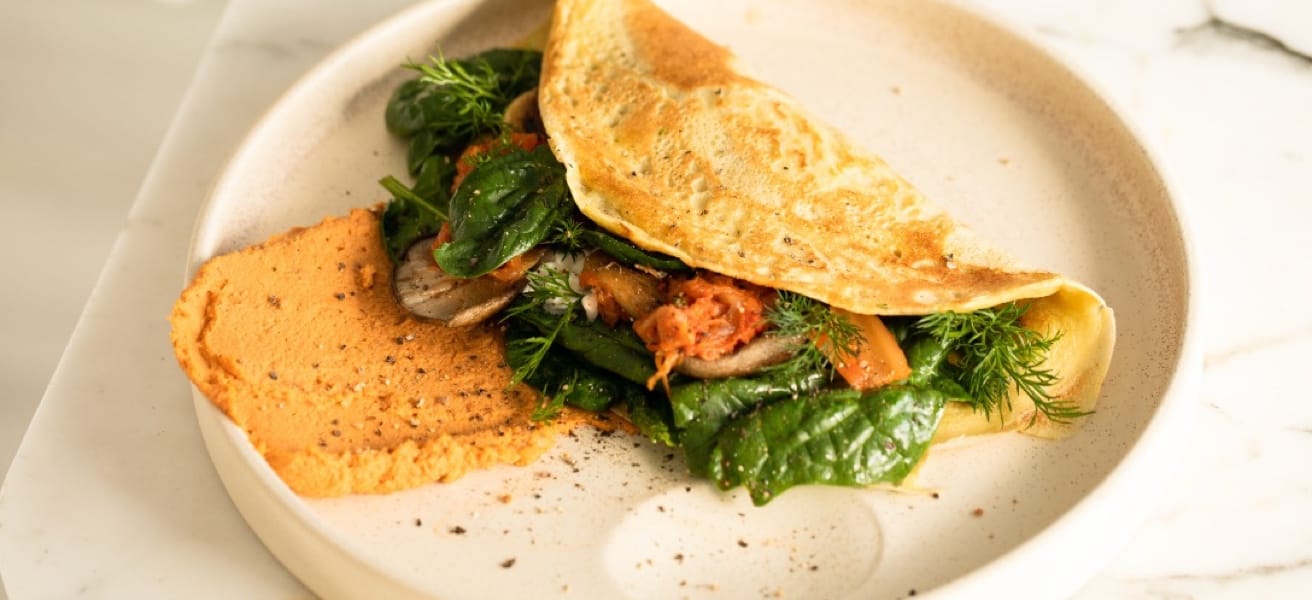 Picture of a folded omelette served on a white plate, with greens, herbs and meat fillings.